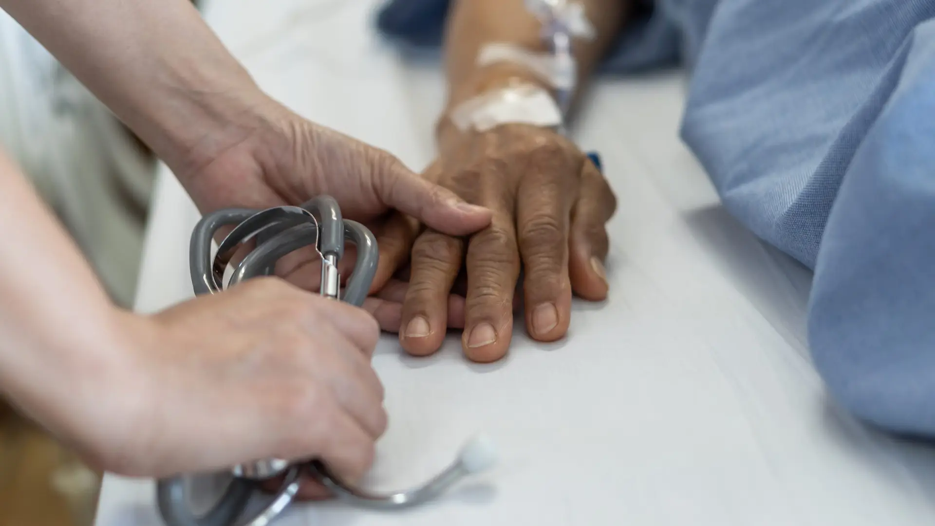 Elderly senior aged patient on bed with geriatric doctor holding hands for trust and nursing health care, medical treatment, caregiver and in-patient ward healthcare in hospital